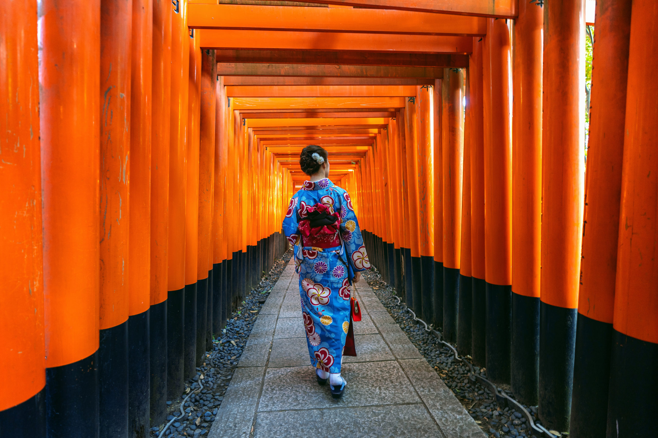 Women in elegant kimonos standing beneath the iconic vermillion torii gates at Fushimi Inari Shrine, one of Kyoto's most famous landmarks with thousands of red gates creating a stunning pathway up the mountain