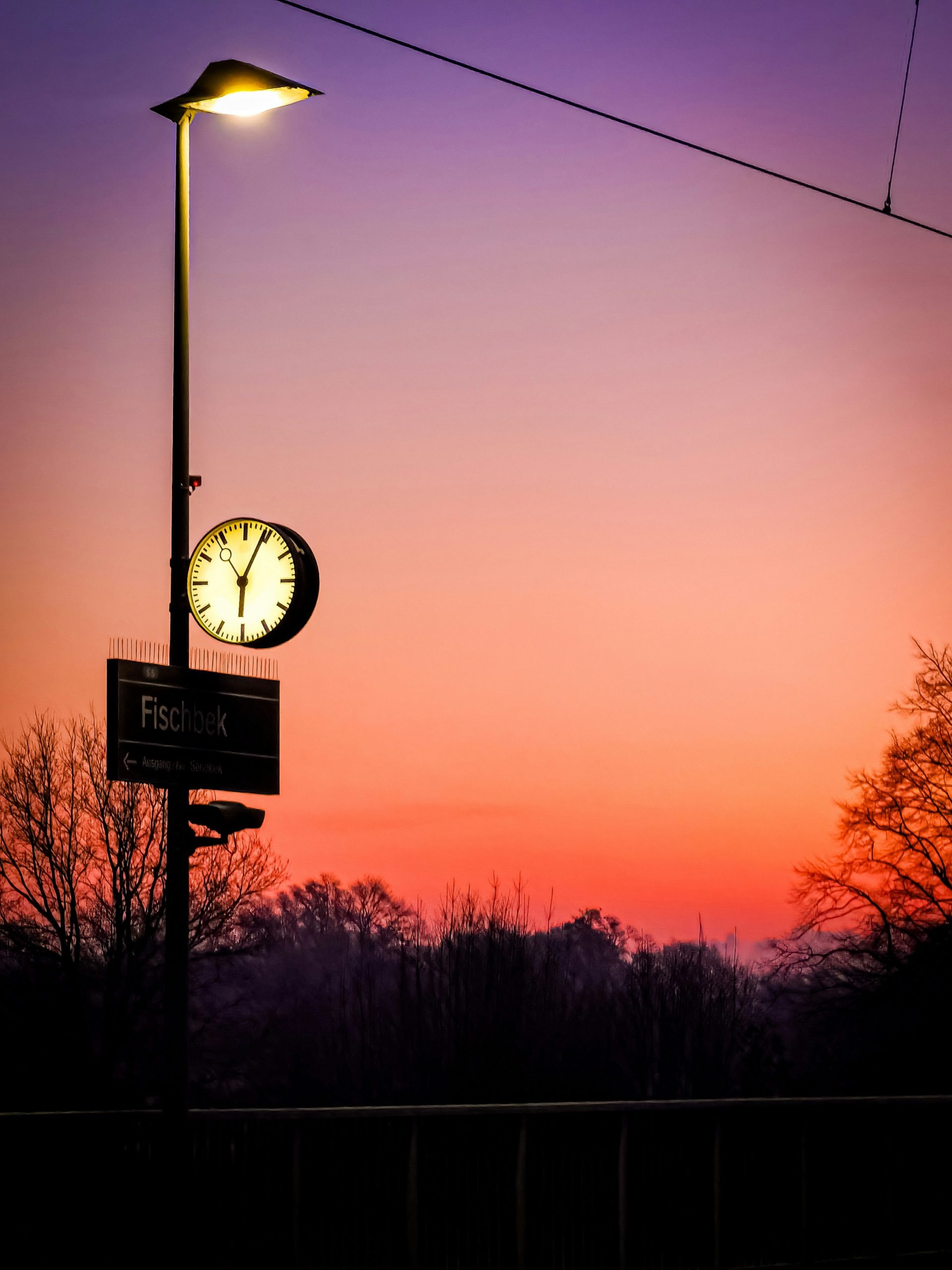 Beautiful sunrise scene with street lamp and clock silhouetted against vibrant purple and orange sky, demonstrating perfect early morning lighting conditions for photography