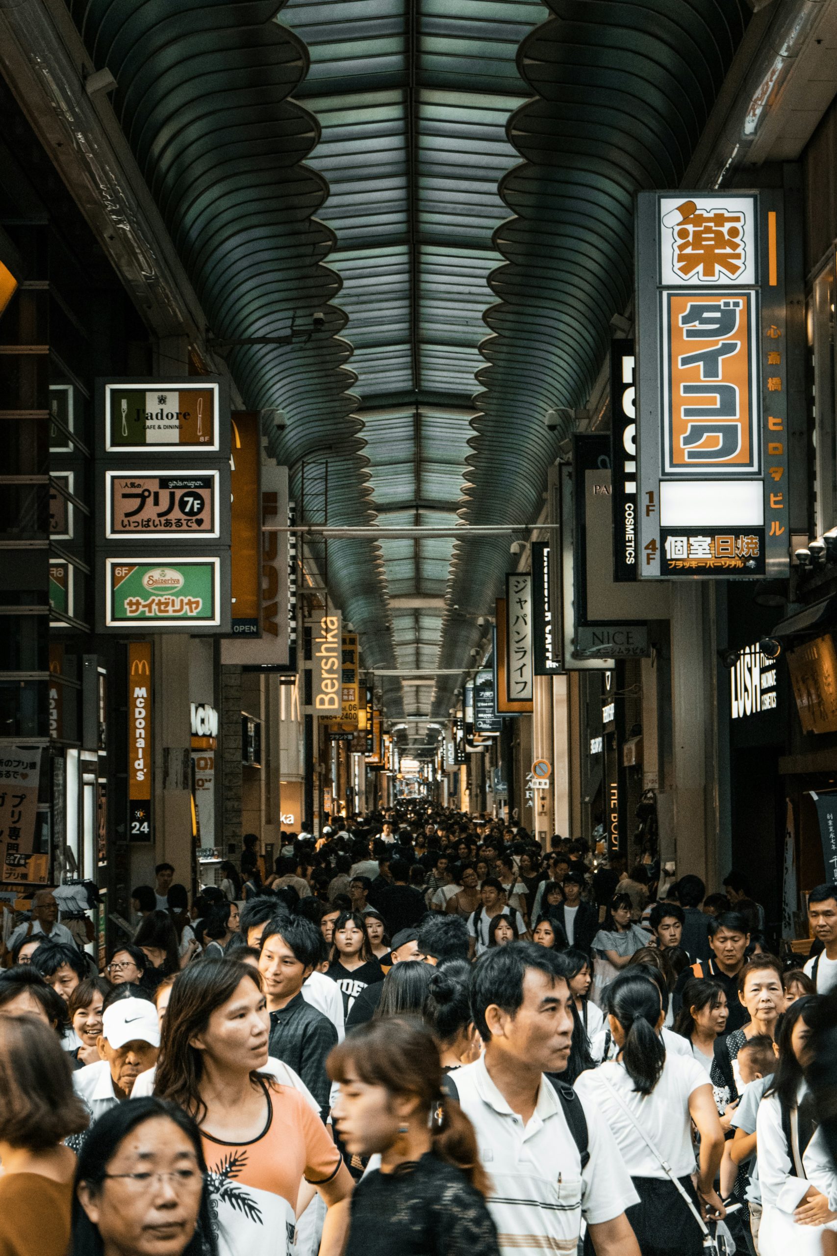 Crowded Japanese shopping street with covered arcade filled with tourists and numerous shop signs, illustrating peak tourist hours to avoid for kimono photography