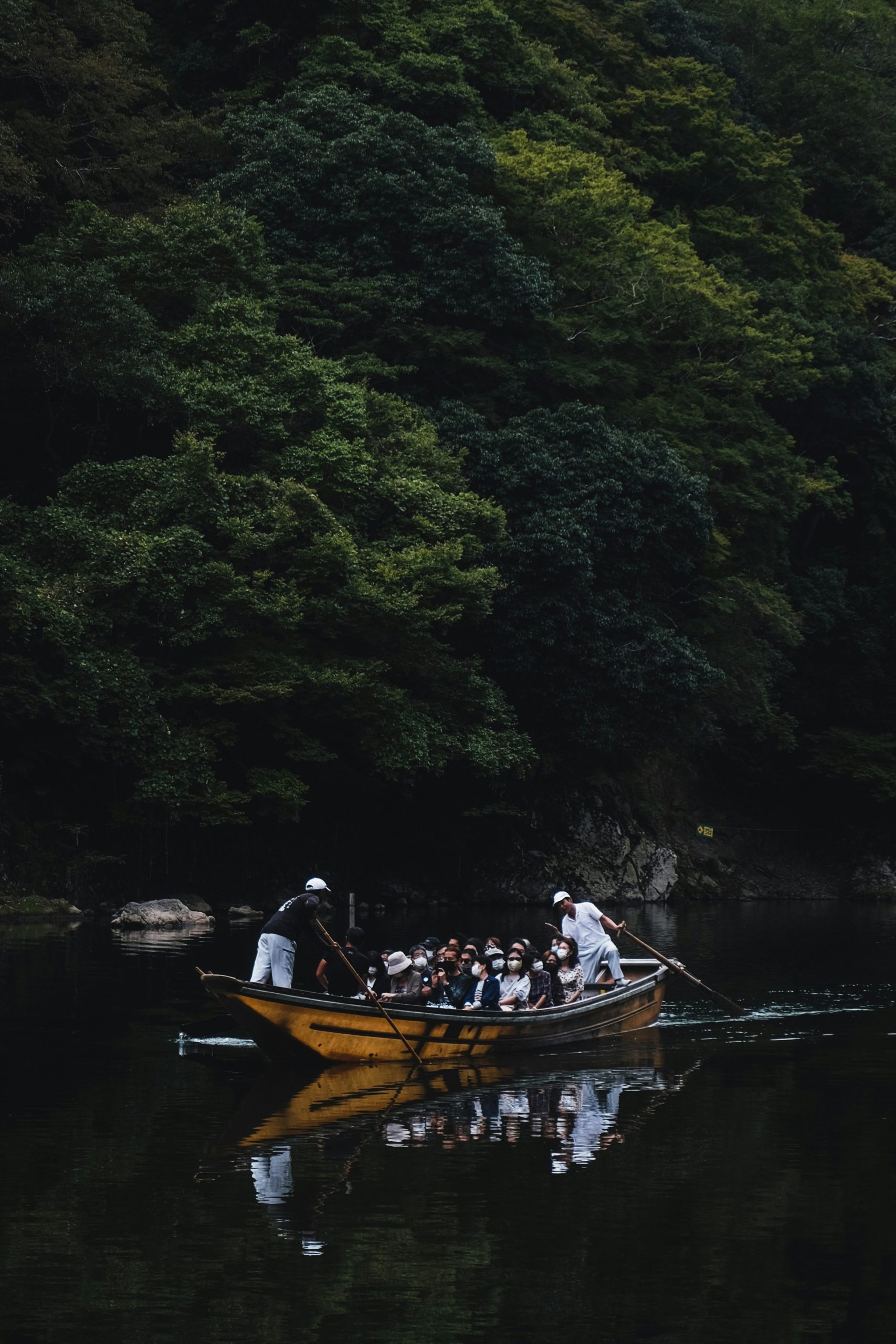 Traditional wooden boat navigating the scenic Hozu River with passengers enjoying the peaceful journey through Kyoto's mountainous landscape